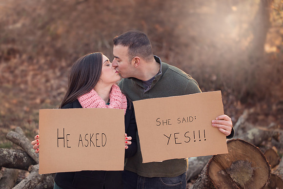 engaged couple kissing and holding cardboard signs