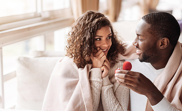 Cheerful African American couple getting engaged in the cafe
