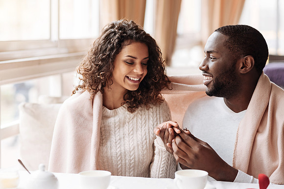 Cheerful young African American couple getting engaged in the caf